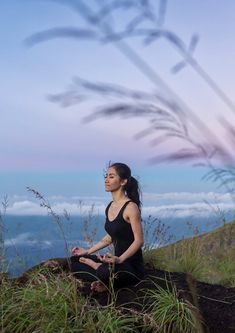 a woman sitting on top of a hill with her eyes closed by an ocean in the background