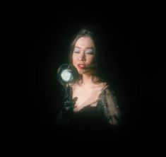 a woman holding a light in her hand while wearing a black dress and dark background