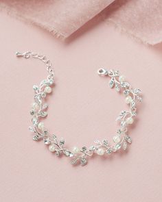 a close up of a bracelet on a pink surface with pearls and crystal beads in the middle