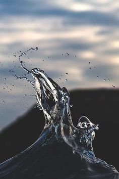 water splashing on top of a wave in the ocean under a cloudy blue sky