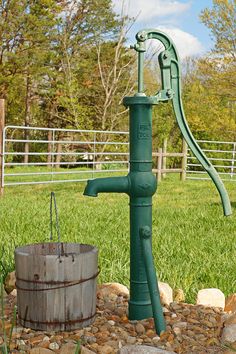 a green water faucet sitting in the middle of a field next to a barrel