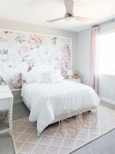 a white bed sitting in a bedroom next to a window with pink flowers on it