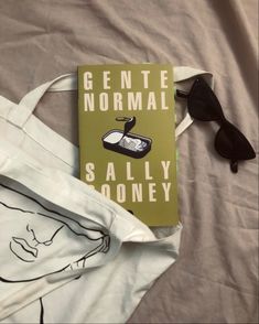 a book sitting on top of a white bag next to sunglasses and a handbag