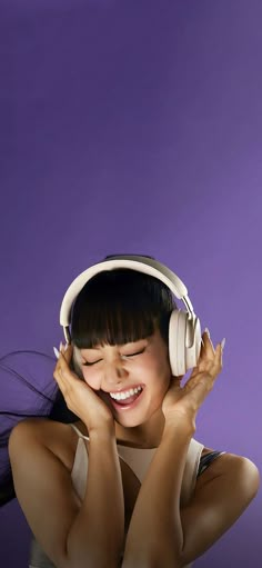 a woman wearing headphones and smiling with her hands on her face, against a purple background