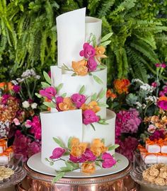 a three tiered cake with flowers on it and other desserts in the background