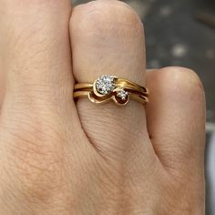 a woman's hand holding a gold ring with two diamonds on top of it