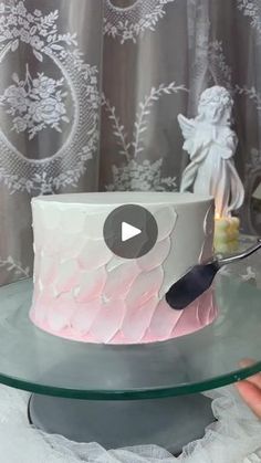 someone is cutting into a pink and white cake on a glass platter with a knife