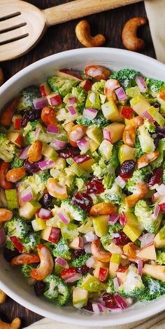 a white bowl filled with broccoli, apples and cranberries next to nuts