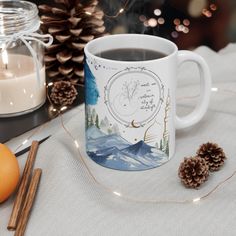 a cup of coffee sitting on top of a table next to pine cones and candles