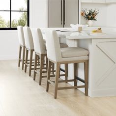 a kitchen with white counter tops and beige bar stools in front of an island