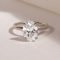 an oval cut diamond sits on top of a white surface with a thin band around it