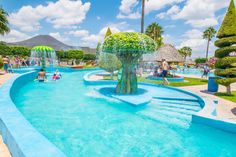 people are playing in the water at an outdoor swimming pool with trees and umbrellas