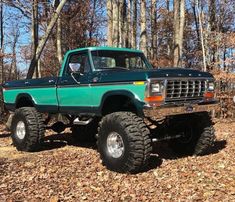 a green truck parked in the woods with big tires on it's front wheels