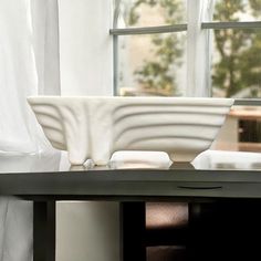 a large white bowl sitting on top of a table next to a window with curtains