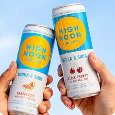 two people hold up cans of high noon sodas in front of a blue sky