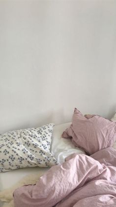 an unmade bed with pink sheets and pillows on top of it, next to a white wall