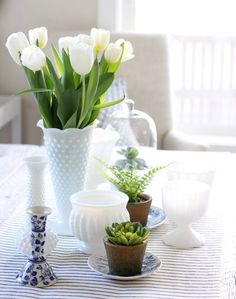 white tulips in vases on a table with succulents and cups