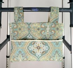 a blue and green paisley purse hanging on a metal rack with two handles in front of a white wall