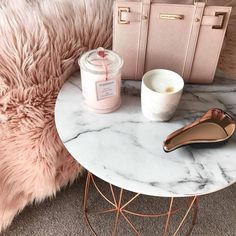 a marble table topped with a pink handbag next to a white cup and brush