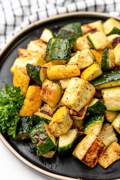 a black plate topped with zucchini and other vegetables