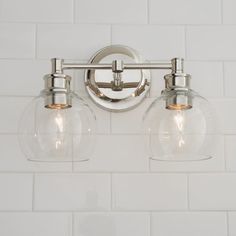 two light bathroom fixture with clear glass globes on the wall and white subway tile