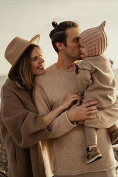 a man and woman holding a baby in their arms while standing next to the ocean