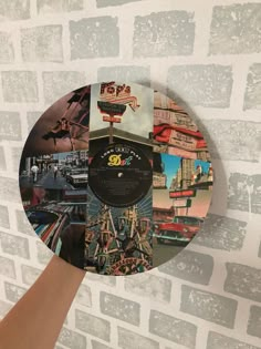 a person holding up a record with pictures on it in front of a brick wall