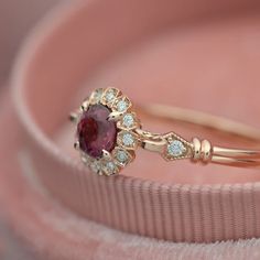 a close up view of a ring with a red stone in the middle and white diamonds around it