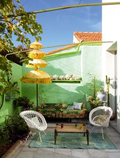 a patio with two chairs and an umbrella in the middle of it, next to a green wall