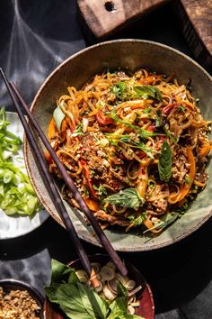 two bowls filled with noodles and vegetables next to chopsticks on a table top