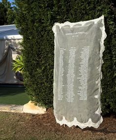 a large white sheet with writing on it sitting in front of a bush and tent