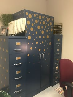 a filing cabinet with gold dots painted on it and a red chair next to it