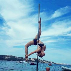 a woman is standing on one leg and holding onto the pole while doing a handstand