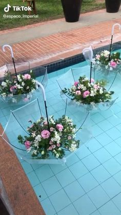 three clear umbrellas with flowers in them sitting on the side of a swimming pool