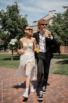 a man and woman walking down a brick walkway holding drinks in their hands while wearing sun glasses