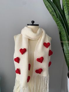 a white scarf with red hearts on it sitting next to a potted plant and a green plant