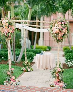 an outdoor wedding ceremony with flowers and greenery on the arch, pink table cloth draped over it