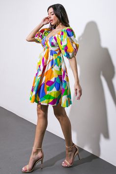 a woman standing in front of a white wall wearing a multicolored dress and heels