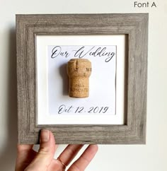 a hand holding a wine cork in front of a white wall with the word our wedding written on it