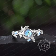 a silver ring with an opal stone in the center and leaves around it, on top of a black surface