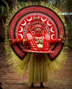 an elaborately decorated mask is displayed in front of a forest background with trees and bushes