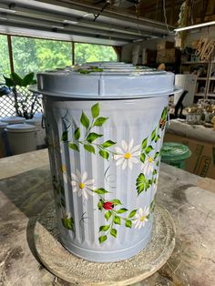 a trash can painted with daisies and ladybugs sitting on top of a table