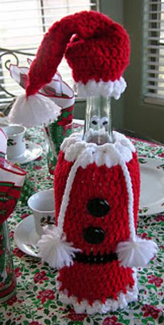 a knitted santa clause hat on top of a glass bottle sitting on a table