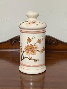 a ceramic jar with flowers painted on it sitting on top of a wooden table next to a wall