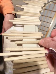 two hands are holding wooden dows in front of a rack with white tiles on it