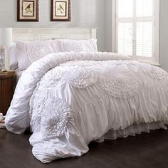 the comforter is white and has ruffles on it, along with two framed pictures