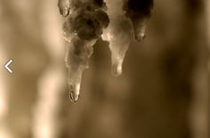 two drops of water hanging from the side of a faucet that has ice on it