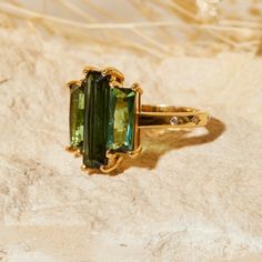 a green ring sitting on top of a white marble surface with gold trimmings