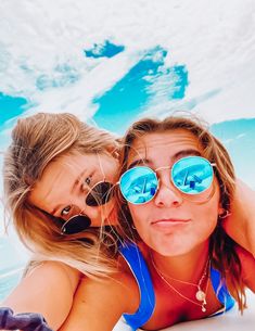 two women are laying on the beach with their arms around each other and looking at the camera