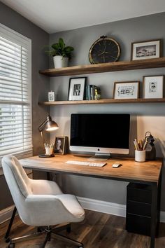 a desk with a computer on it in front of a window and some framed pictures